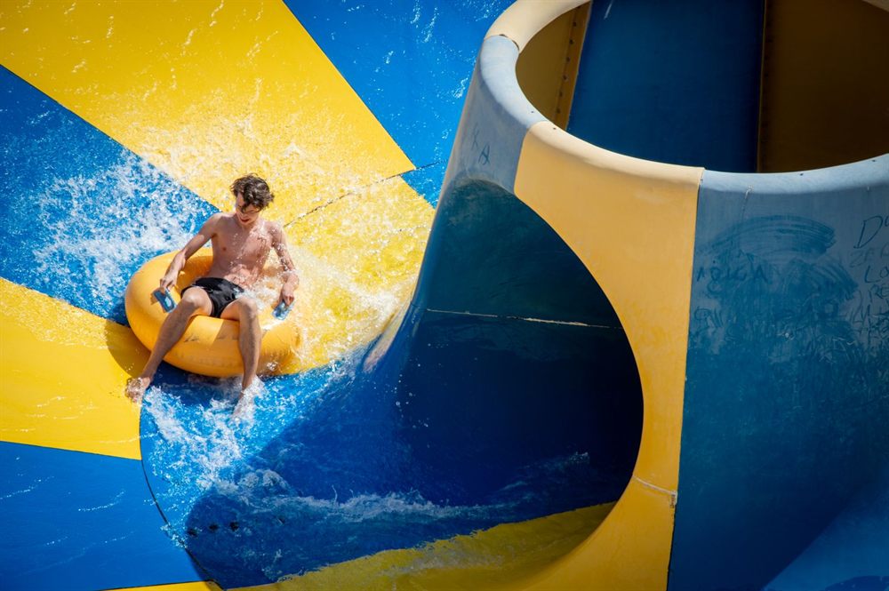 Teen riding an inflatable ring down a blue and yellow waterslide