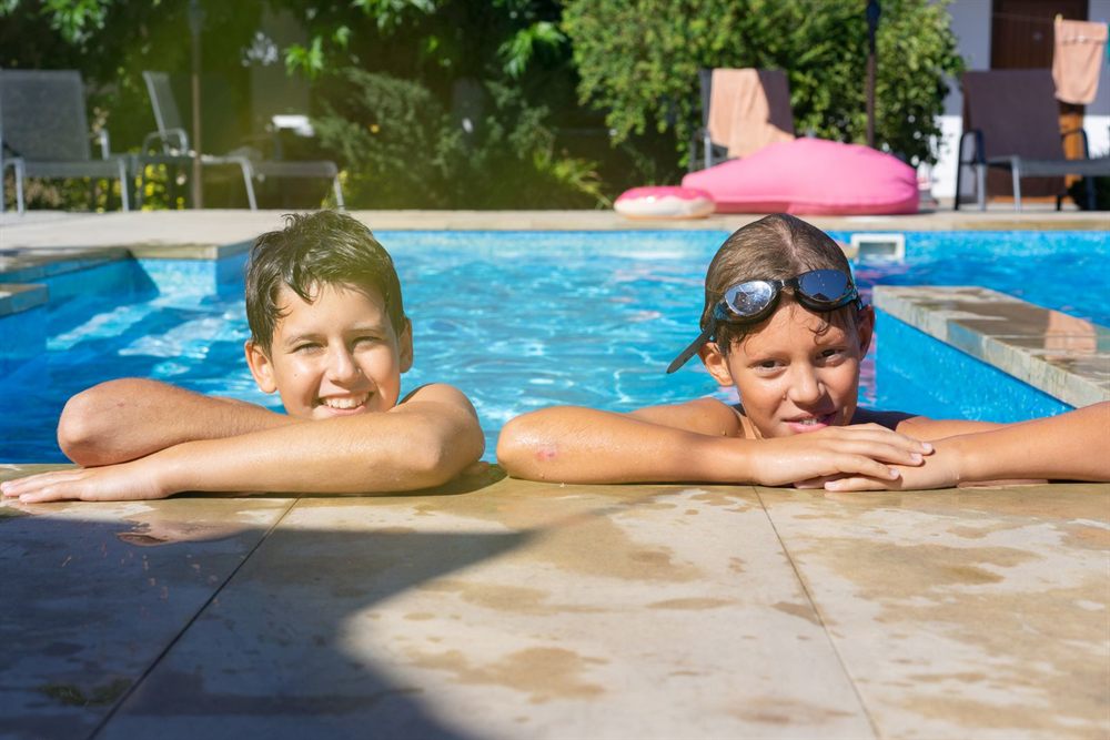 Two smiling boys resting their arms on the edge of a pool
