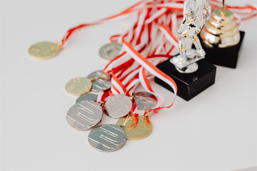 Gold and silver medals with ribbons beside small trophies