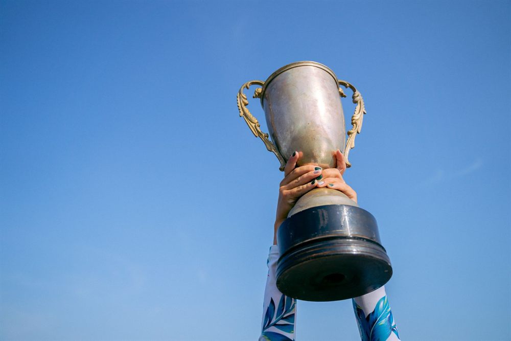 Hands raising a silver trophy cup against a blue sky